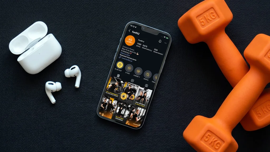 Funfit II: profil klubu fitness na Instagramie w telefonie obok hantli