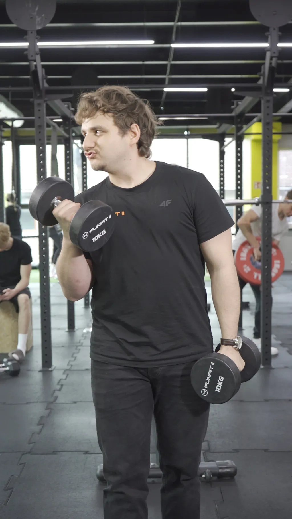 Mężczyzna z hantlami na siłowni, surowy kadr z reklamy Funfit II przed korekcją barwną