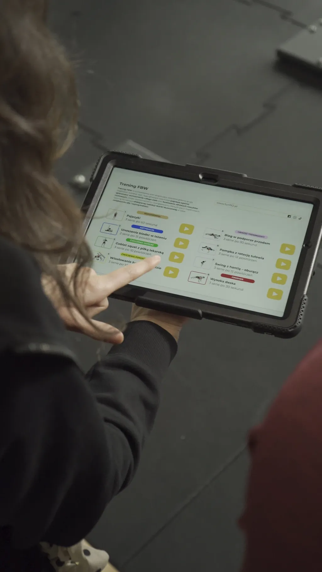 Plan treningowy FBW na tablecie w dłoniach trenerki, kadr Funfit II przed korekcją barwną
