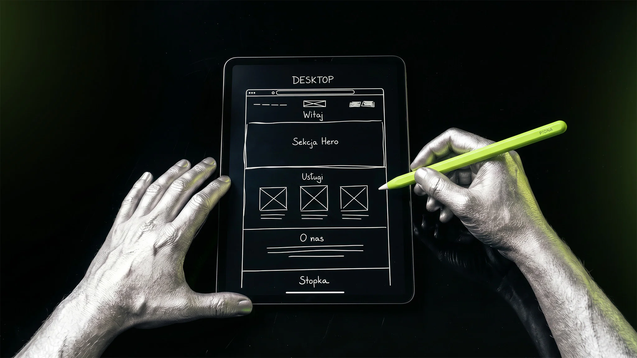 Srebrne dłonie rysują na tablecie wireframe strony internetowej: hero, usługi, o nas i stopka
