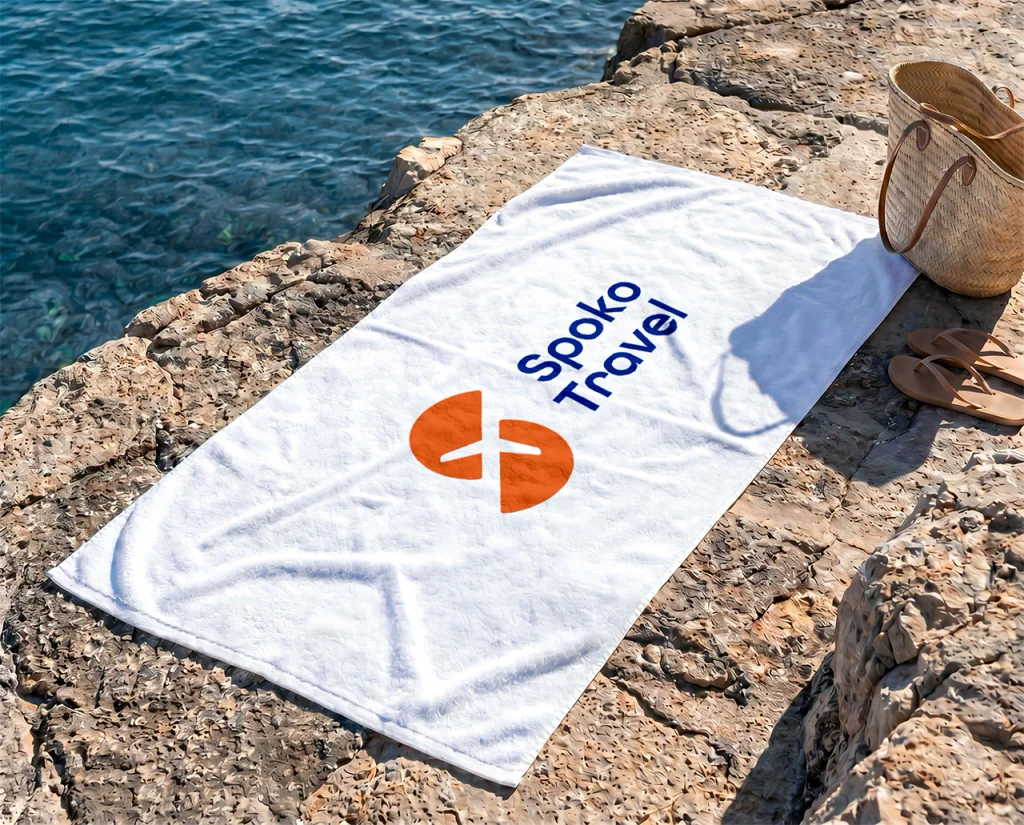 Spoko Travel: ręcznik plażowy z logo na nadmorskich skałach, element identyfikacji wizualnej